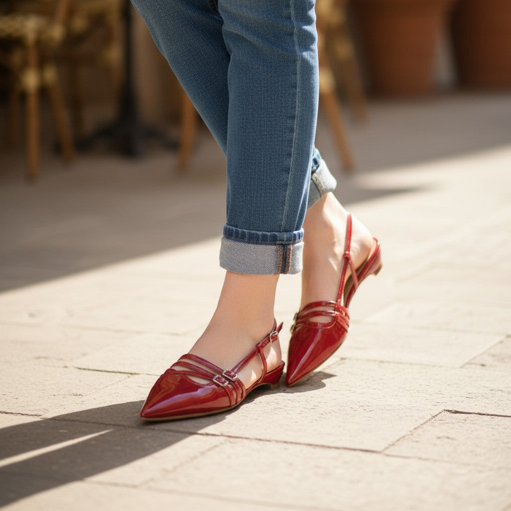 Inscarpa red patent leather women's flat sandals with buckle detail, paired with blue jeans and a black t-shirt.